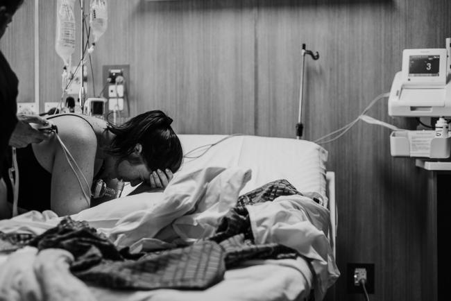 Black and white image of a mother leaning over the hospital bed in labour during a Perth birth photography session