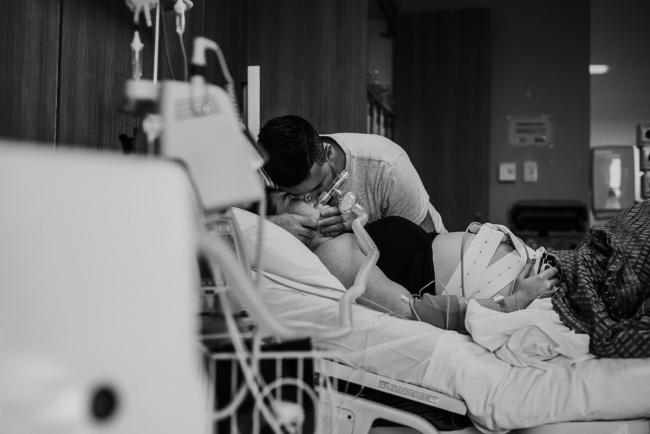 Black and white image of the gas cord leading to a man hugging his partner's head during a Perth birth photography session