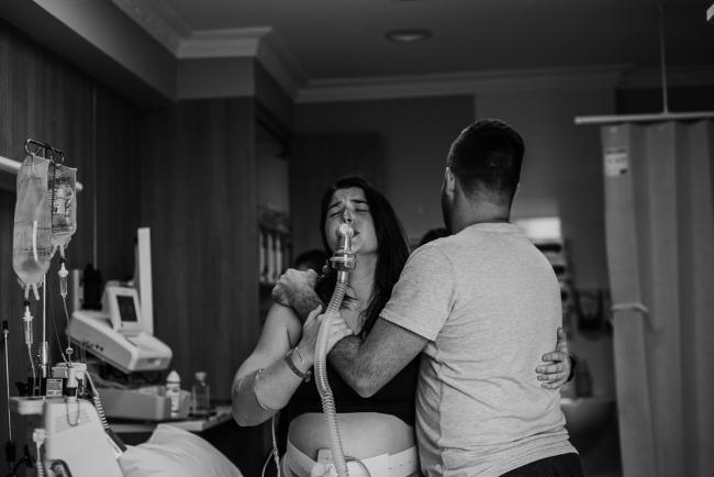 Black and white image of a man and woman holding onto each other as she labours during a Perth birth photography session