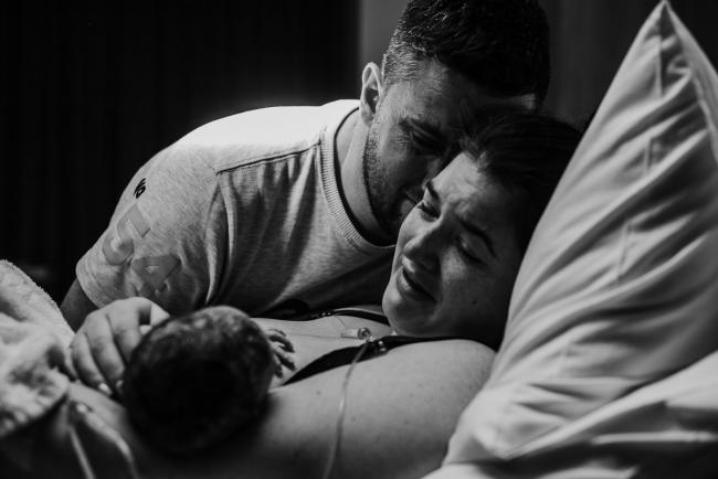 Black and white image of a couple crying and looking down at their new baby during a Perth birth photography session