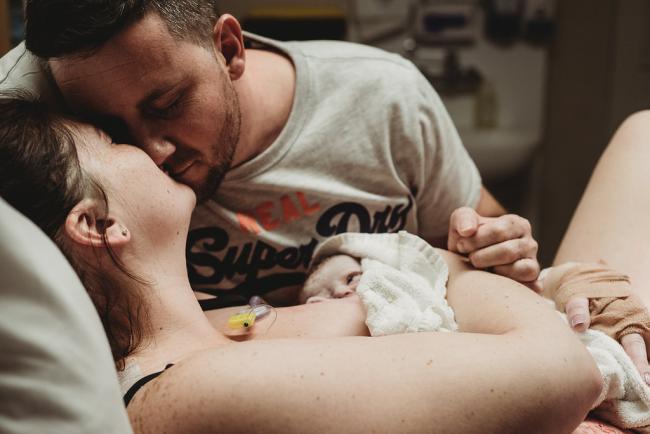 Couple kissing as they cradle their new baby during a Perth birth photography session
