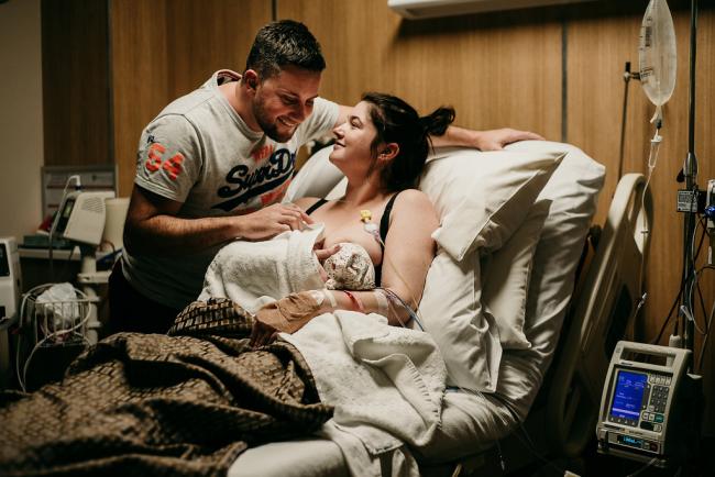 Couple smiling at each other and their new baby on a hospital bed during a Perth birth photography session