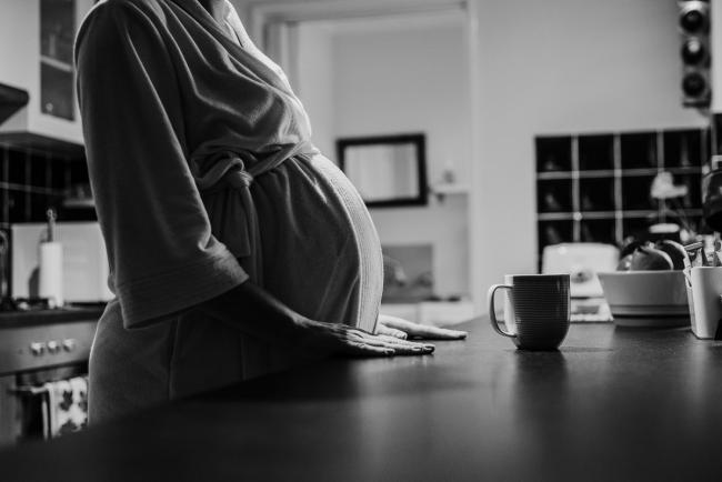 black and white image of pregnant woman resting her hands on the kitchen bench during in-home maternity photography Perth session