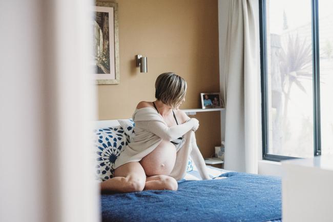 Pregnant woman sitting on her bed during in-home maternity photography Perth session