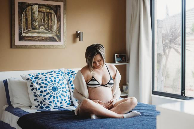 Pregnant woman sitting on her bed during in-home maternity photography Perth session