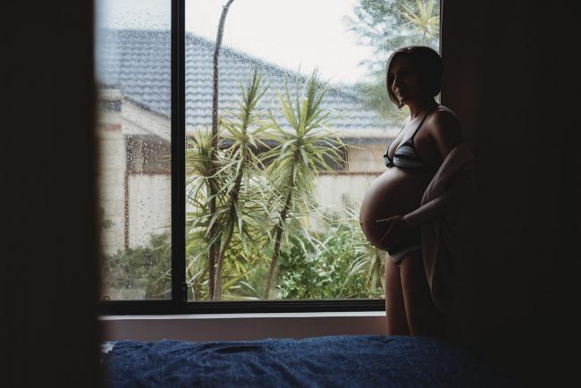 Pregnant woman standing by the window during in-home maternity photography Perth session