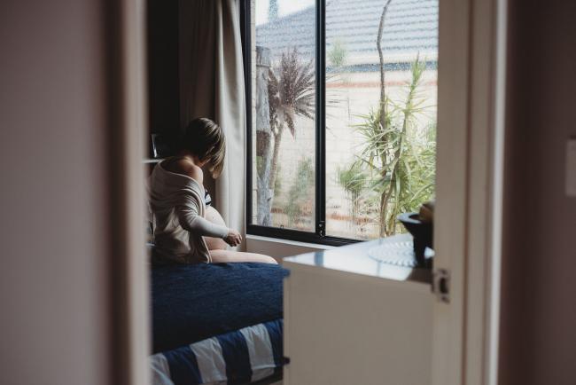 Pregnant woman sitting on her bed during in-home maternity photography Perth session