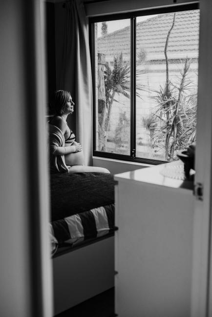 Pregnant woman sitting on her bed during in-home maternity photography Perth session