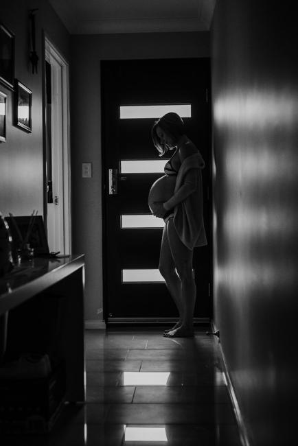 Pregnant woman standing in front of her door during in-home maternity photography Perth session