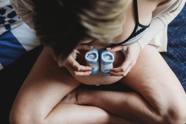 Top down image of pregnant woman placing blue booties on her tummy during in-home maternity photography Perth session