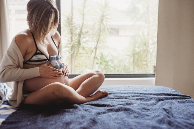 Pregnant woman sitting on her bed during in-home maternity photography Perth session