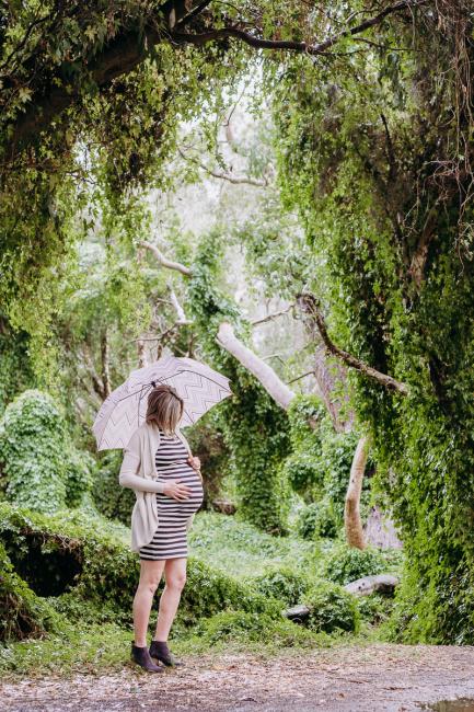 Pregnant woman standing with umbrella during maternity photography Perth session at The Secret Garden