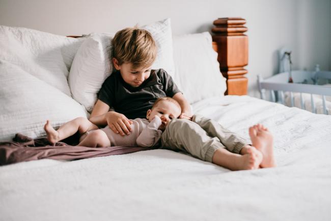 20180610-20180610-DSC_8104 Little boy sitting on the bed holding his new baby sister during lifestyle newborn photography Perth session