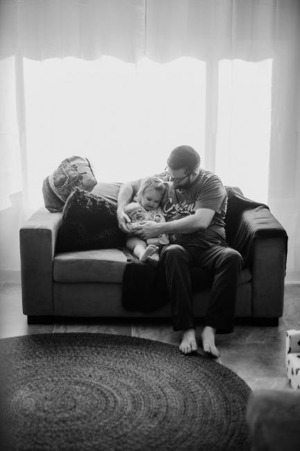 20180720-DSC_8626 black and white image of father sitting on the couch with his two daughters during lifestyle newborn photography Perth session