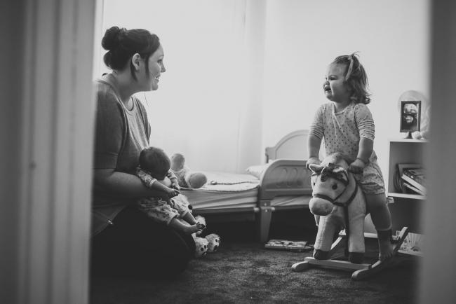 20180720-DSC_8981 black and white image of mother holding her new baby while talking to her toddler who is on a toy horse during lifestyle newborn photography Perth session