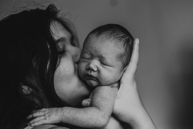 black and white image of mother kissing new baby during lifestyle family photography Perth session