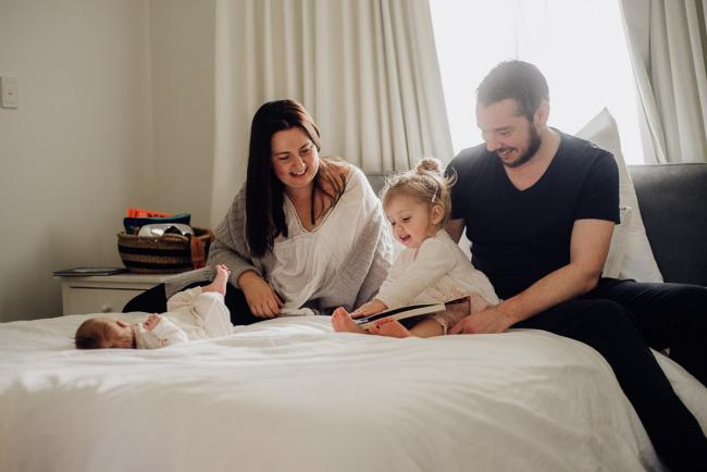 family of 4 sitting on their bed reading a book during lifestyle newborn photography Perth session