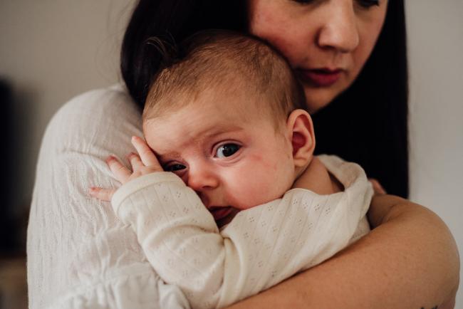 Little baby being held by her mum and looking at the camera during lifestyle newborn photography Perth session