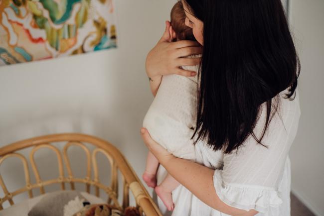 Mother holding her baby and about to place her in the bassinet during lifestyle newborn photography Perth session