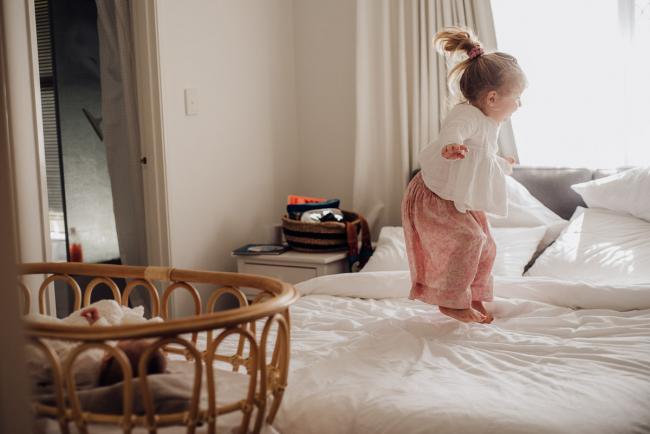 Little girl jumping on the bed during lifestyle newborn photography Perth session