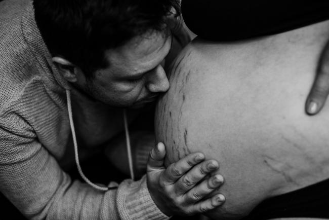 black and white image of man kissing his pregnant wife's tummy during Perth birth photography session