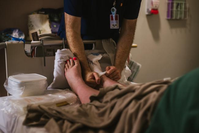 Midwife putting stockings on a mum before a c-section during Perth birth photography session