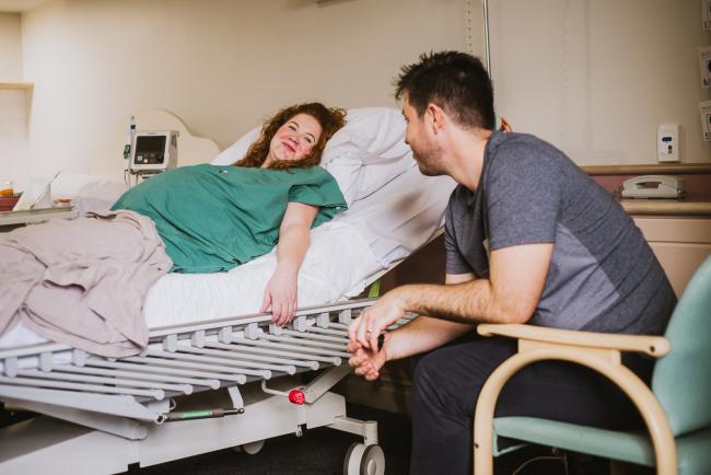 Pregnant woman laying in hospital bed smiling at her partner during Perth birth photography session
