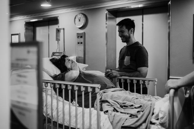 black and white image of pregnant mother in hospital bed with her partner by her bed during Perth birth photography session