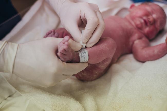Midwife placing hospital tag on new baby's foot during Perth birth photography session