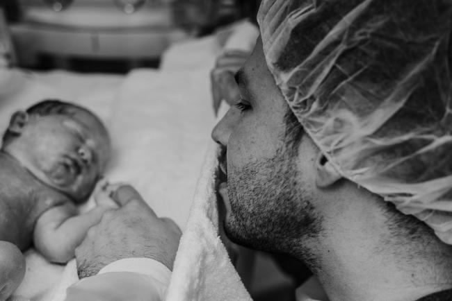 black and white image of father holding his new baby's hand during Perth birth photography session