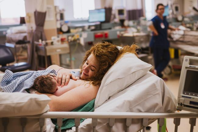 Mother on hospital bed attempting a first breastfeed with her new baby during Perth birth photography session
