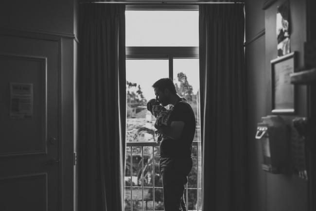 20180809-DSC_6475 black and white image of father kissing new baby in front of hospital window during Fresh 48 photography Perth session