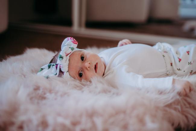 Baby laying on a pink blanket with a floral bow in her hair during a Perth newborn photography session