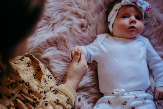 Big sister holding onto her baby sister's hand whilst laying on a pink blanket during a Perth newborn photography session