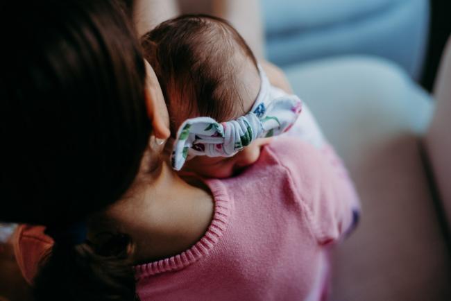 Baby's head resting on her big sisters shoulder who is carrying her during a Perth newborn photography session