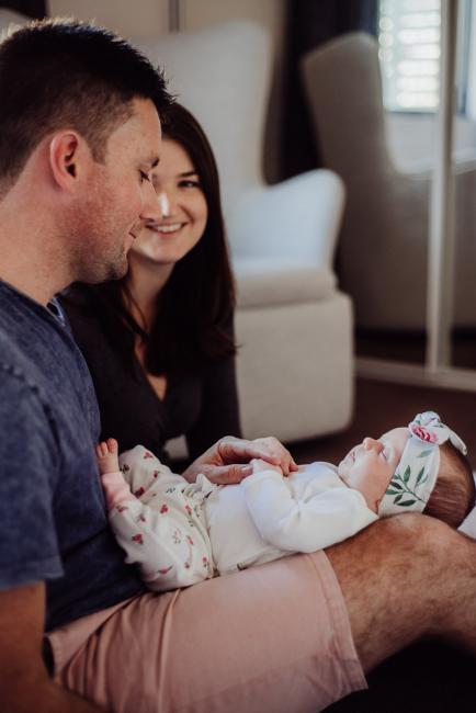 New baby laying on her dad's lap while her mum is sitting next to them and smiling at her dad during a Perth newborn photography session