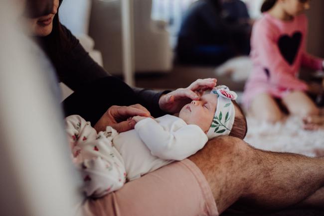 New baby laying on her dad's lap while her mum touchers her nose during a Perth newborn photography session
