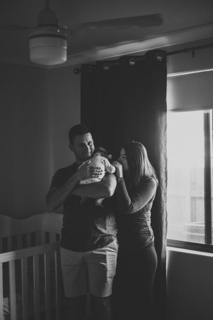 Black and white image of a couple standing in the nursery with dad holding their new baby daughter during a Perth newborn photography session