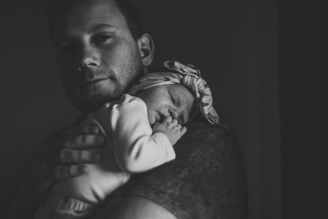 Black and white image of a baby laying on her dad's shoulder, and dad smiling at the camera during a Perth newborn photography session