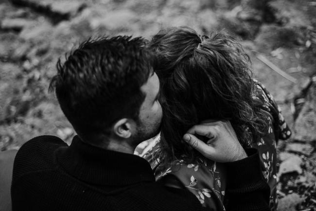 Black and white image of a couple from behind as the man kisses his wife on the cheek during a maternity session in Perth