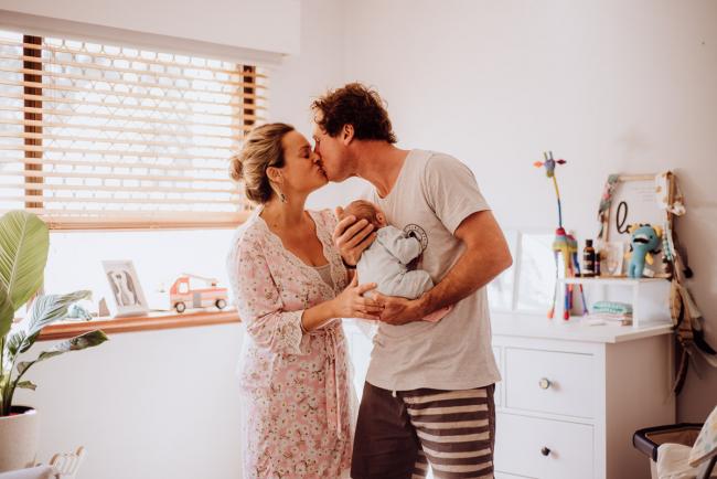 Couple kissing whilst holding their new baby in the nursery during a Perth newborn photography session