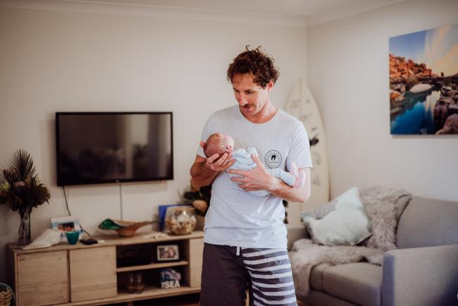 Dad standing in the lounge room holding onto his new baby during a Perth newborn photography session