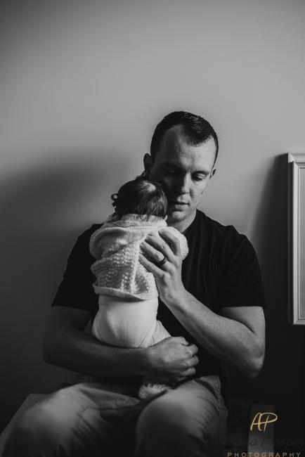 Black and white image of a dad holding his new baby whilst sitting on a chair during a Perth newborn photography session