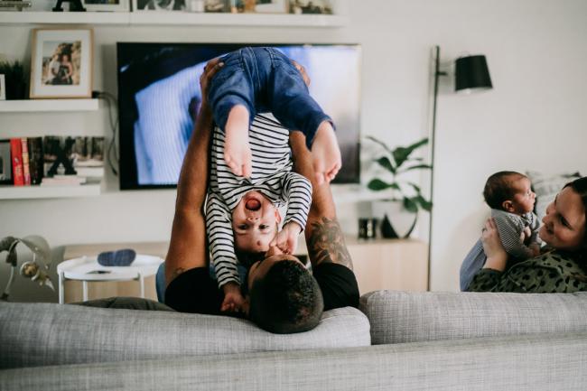 Family sitting on the couch as dad lifts his laughing son upside down during a Perth newborn photography session