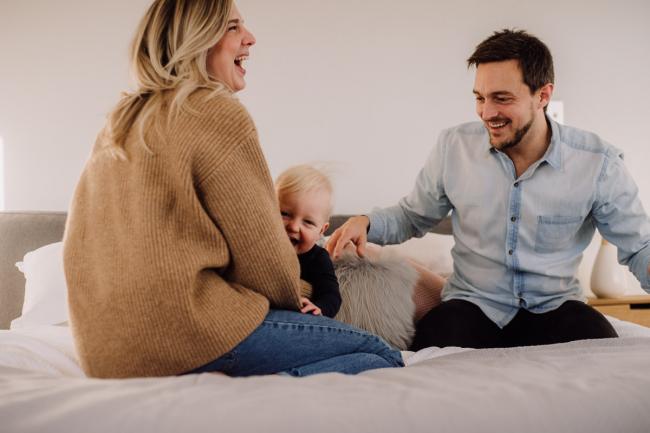 Mum and dad on the bed with their son as the dad begins to tickle his son during a Perth in-home family lifestyle session