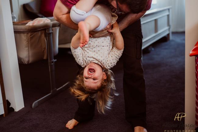 Dad lifting his laughing daughter upside down during a Perth newborn photography session