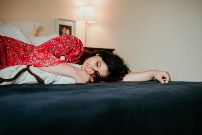 Mother laying across the bed with her baby, eyes closed and arm outstretched, during a Perth newborn photography session