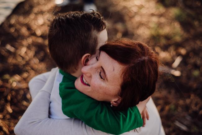Little boy wrapping his arms around his mum as she smiles and closes her eyes during a family photography session at The Pines Wanneroo in Perth