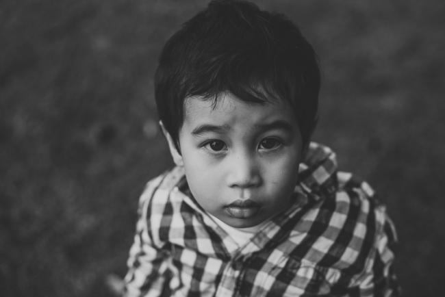 Black and white image of a little boy looking seriously at the camera during a family photography session at Hyde Park, Perth