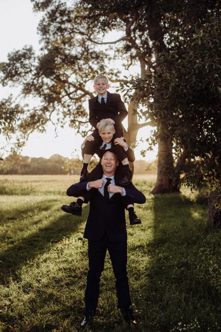 20180909-DSC_5155-1 Father carries one son on his shoulder, who carries his younger brother on his shoulder during golden hour family photography Perth session at Perry's Paddock